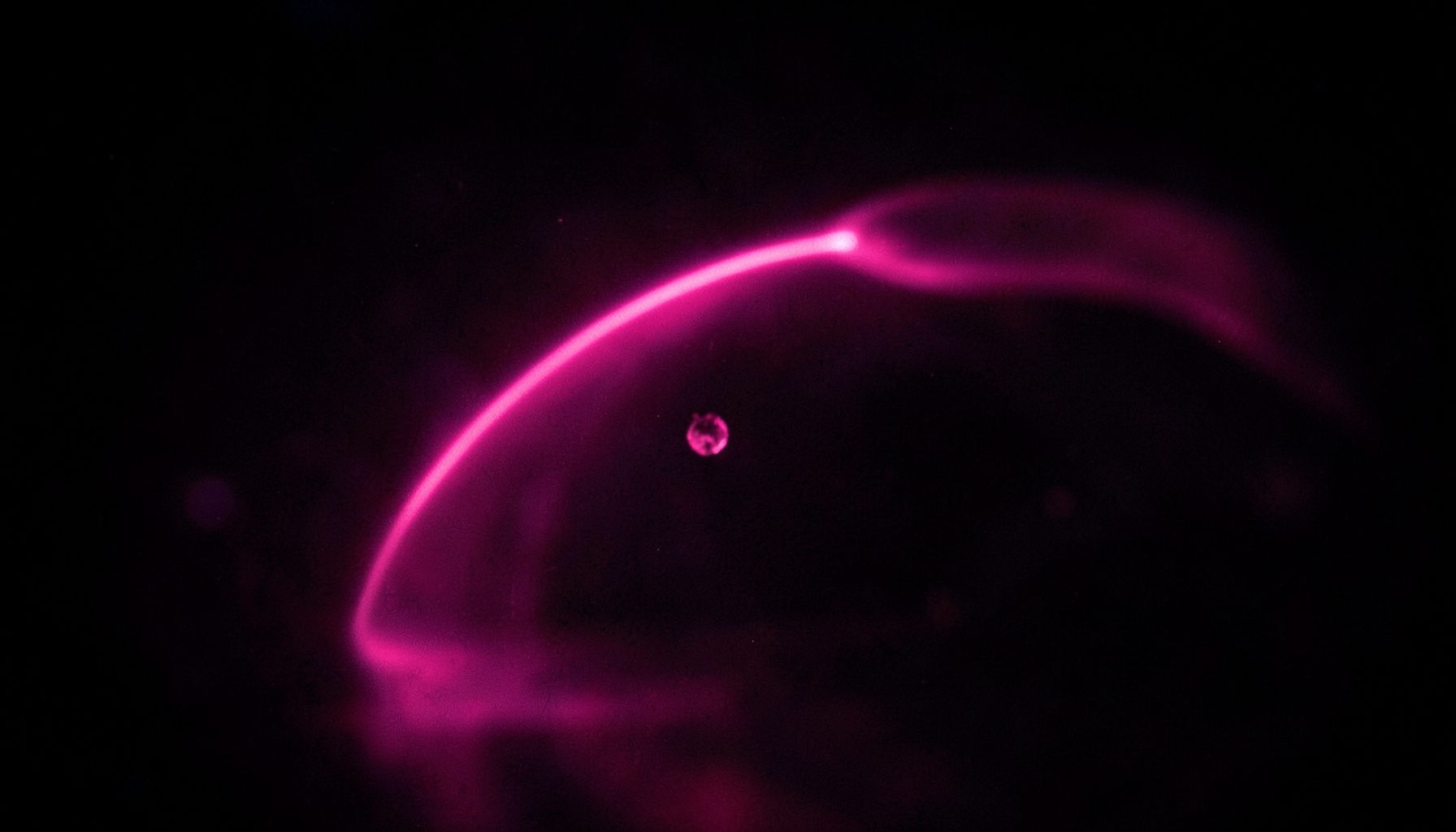 Dark scene with a glowing pink trajectory arc and a small object in motion, suggesting physics simulation